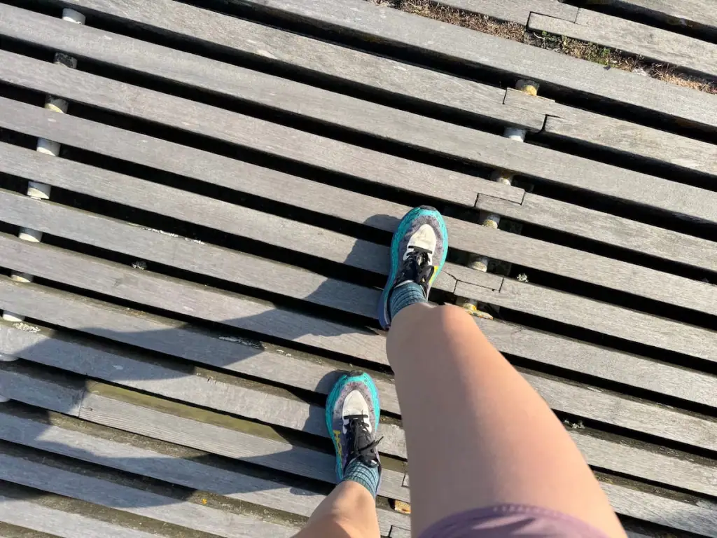 View from above of two legs walking along a boardwalk on the Camino Portugués Coastal route with Hoka Speegoat shoes on the feet.
