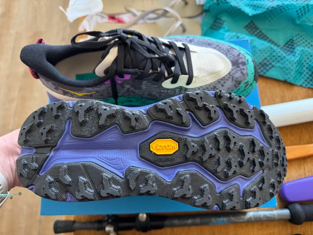 Brand new Hoka Speedgoat 6 shoes sitting on top of the box with one flipped over so you can see the tread on the bottom.