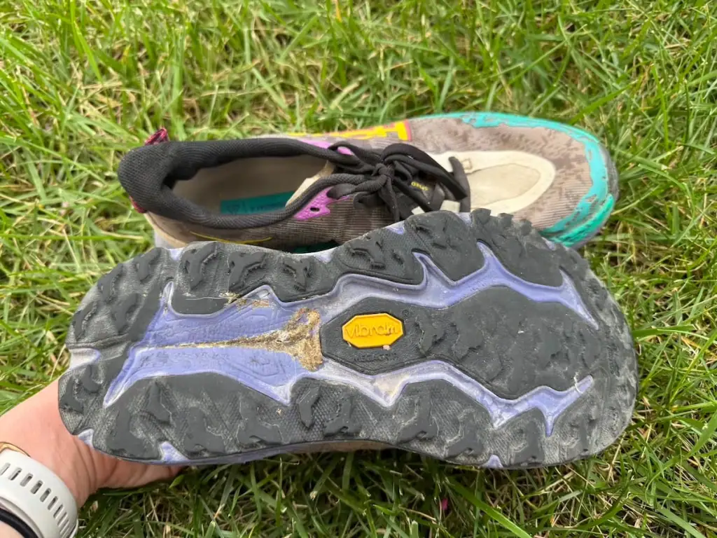 Used Hoka Speedgoat 6 shoes sitting on top of the box with one flipped over so you can see the tread wearing down in some areas on the bottom.