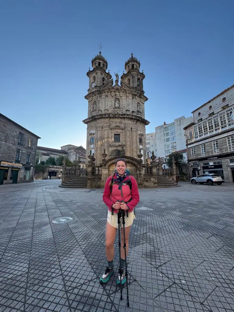 Mikala smiling with her hiking poles and backpack standing in front of the main church in Pontevedra on the Camino Portugués Central route.