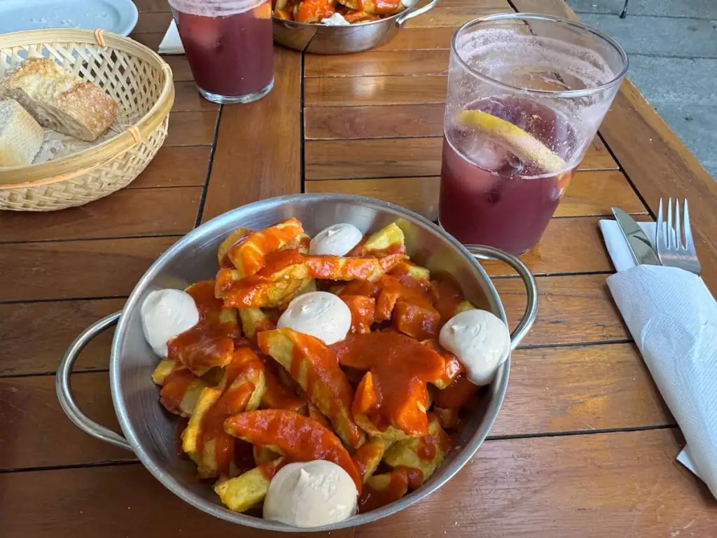 Bowl of patatas bravas and a glass of tinto de verano on a wooden table.