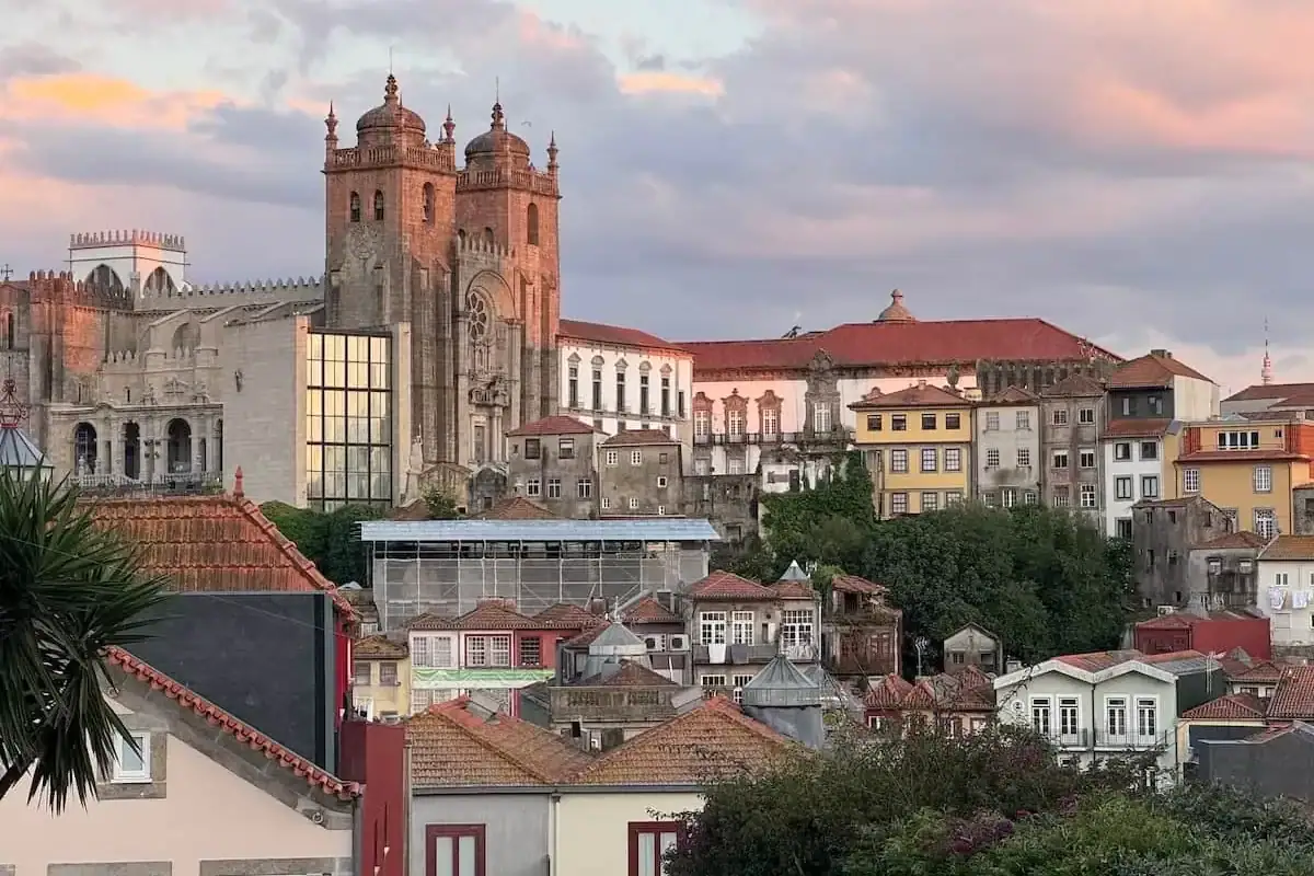 Porto Cathedral sitting on top of a hill with buildings below and glowing in the pink light of sunset.