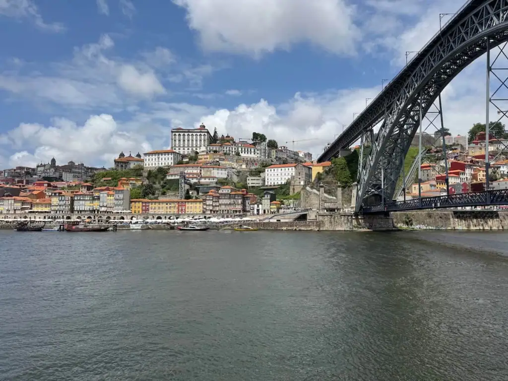 The Dom Luís I Bridge on the right over the Douro River in the foreground with the city center of Porto, Portugal built up on hills behind.