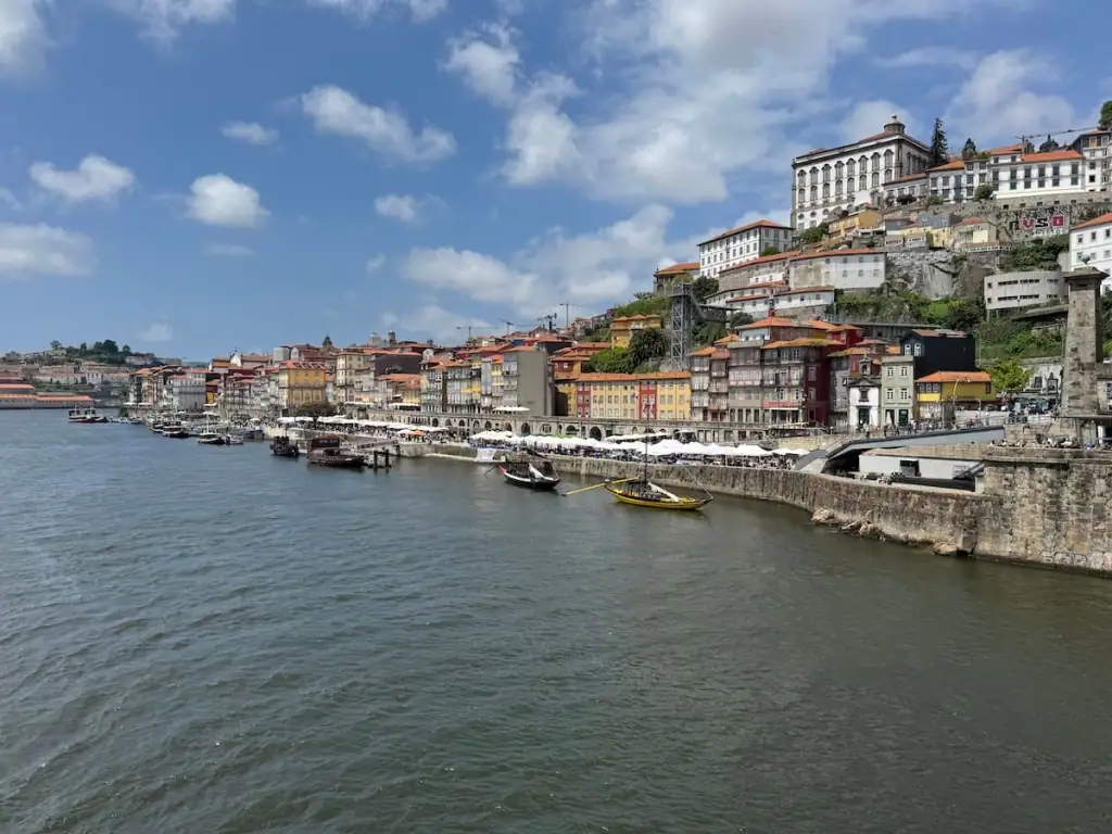 View of Porto, Portugal's city center on the other side of the Douro River from the Dom Luís I Bridge on a sunny day with blue skies and a few white clouds.