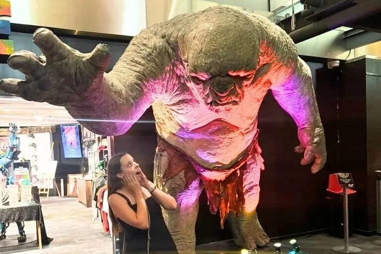 Mikala standing pretending to be scared in front of a massive The Lord of the Rings troll statue at Wētā Cave at Wētā Workshop Unleashed in Auckland.
