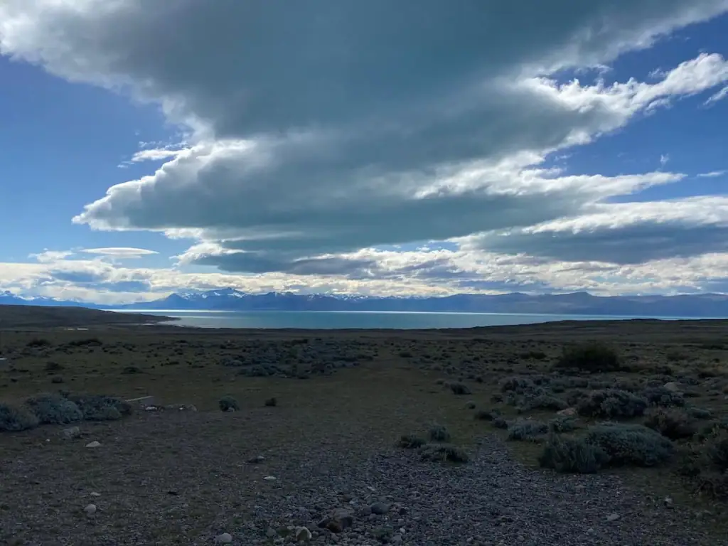 Dramatic Patagonian landscape with low brush, rocky terrain, and a wide sky over Lake Argentino from just outside of El Calafate with the Andes in the distance.
