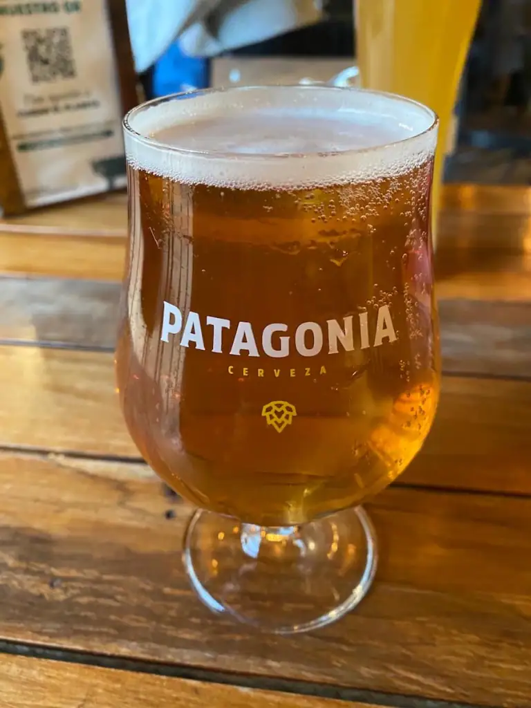 A cold glass of amber beer on a wooden table at Patagonia Brewing, with branding etched on the glass.