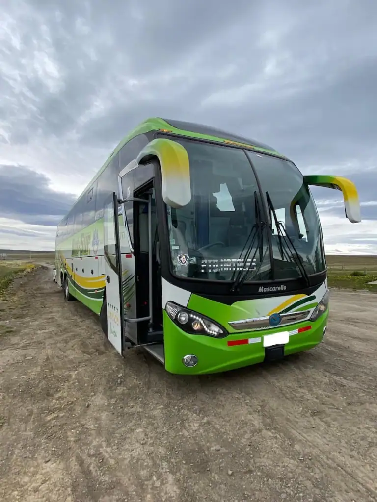 A bright green long-distance bus from El Calafate, Argentina to Puerto Natales, Chile parked on a dirt road under cloudy skies in Patagonia. Buses are a great transportation method to consider for your itinerary to Argentina.