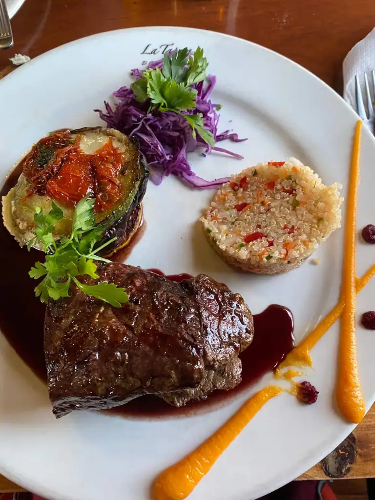 Elegant plate of steak with red wine sauce, quinoa salad, roasted vegetables, and garnishes served at La Tapera restaurant in El Chaltén.