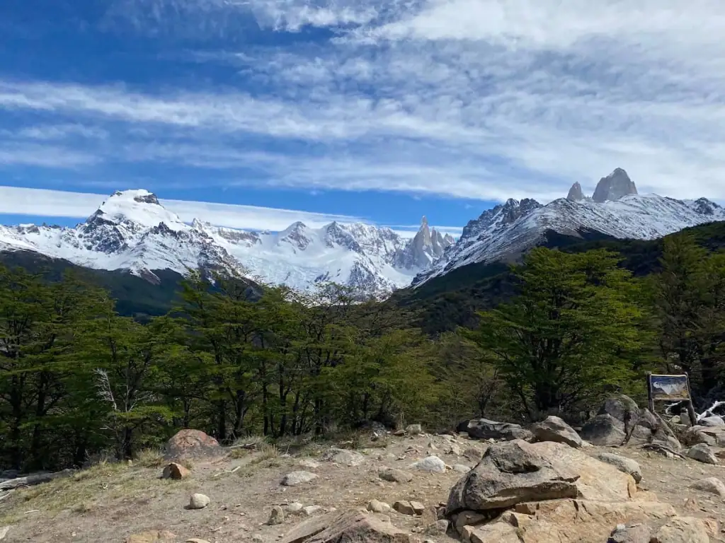 Panoramic view of snow-covered peaks and dramatic spires in Los Glaciares National Park on the Laguna Torre hike, with Fitz Roy and surrounding mountains rising above green forest.