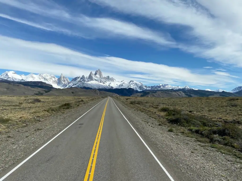 Open highway stretches toward the snow-covered peaks of Mount Fitz Roy under a wide sky in Patagonia on the way to El Chaltén.
