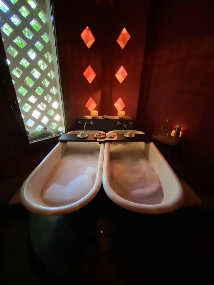 Two clawfoot bathtubs filled with bubbles in a candlelit spa at a hotel in Mendoza, with red walls and geometric light fixtures. A relaxing spa experience offers a luxurious break during a 2-week Argentina itinerary.