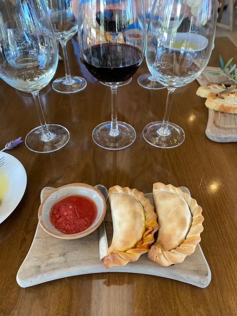 Traditional Argentine empanadas served with red sauce on a wooden board, set in front of several wine glasses at a tasting table at Trapiche Winery in Mendoza. I loved my lunch at this winery and definitely think any visit to Mendoza deserves a winery lunch.