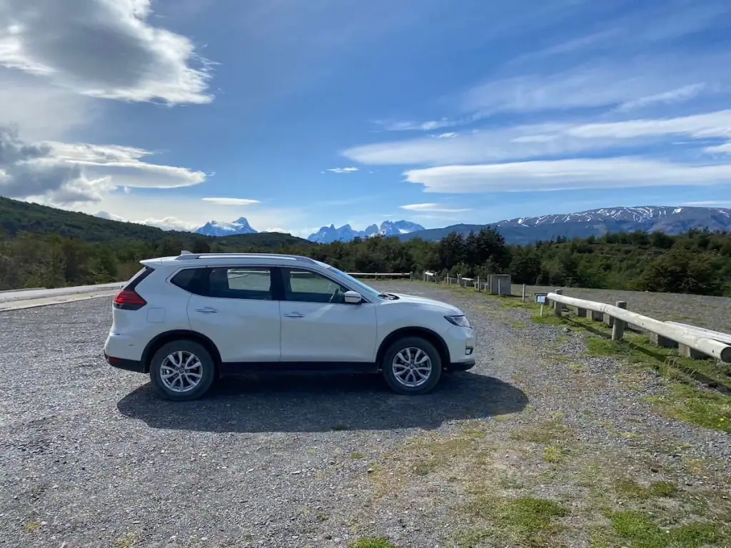 White SUV parked at a scenic overlook on the way to Torres del Paine, Chile with snowy peaks and blue skies in the background.