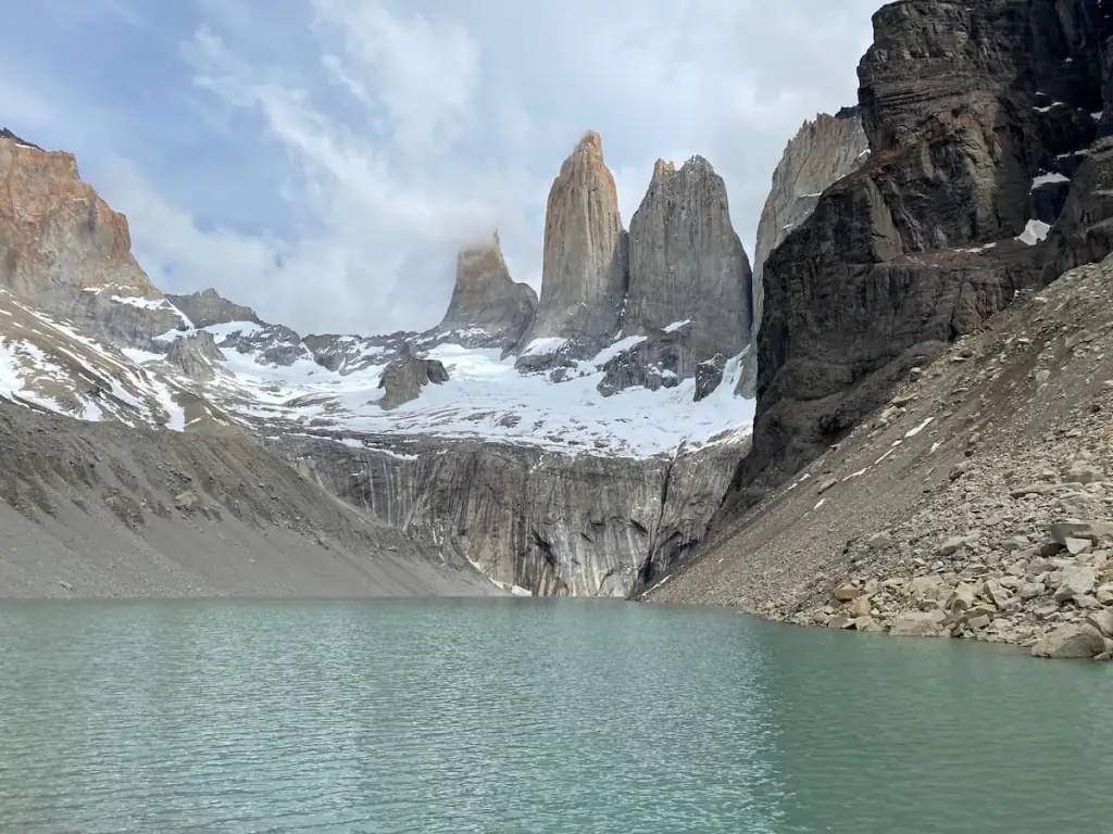 Iconic granite towers of Torres del Paine rise sharply above a milky green glacial lake, surrounded by snow-dusted cliffs and rocky slopes. This dramatic viewpoint is a must-visit for adventurous travelers on a 2-week Argentina itinerary that includes a detour into Chilean Patagonia.