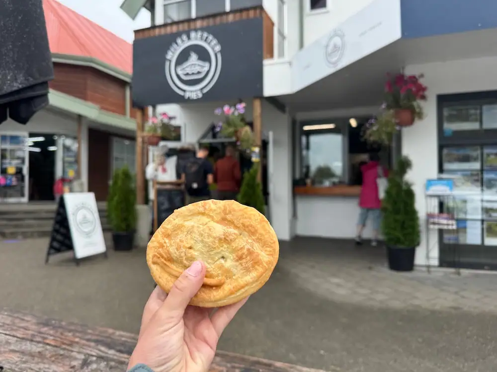 Mikala holds a freshly baked pie in front of the entrance to Miles Better Pies in Te Anau. Sampling one of the town's famous savoury pies is one of the tastiest things to do in Te Anau.