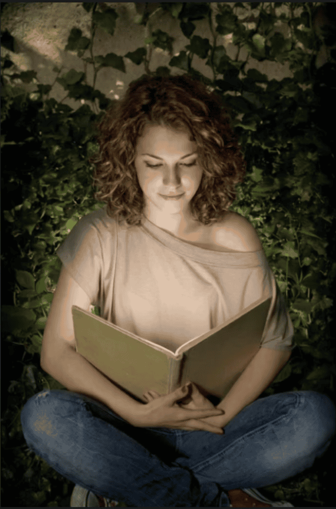 Woman reading a book outdoors at night surrounded by greenery.