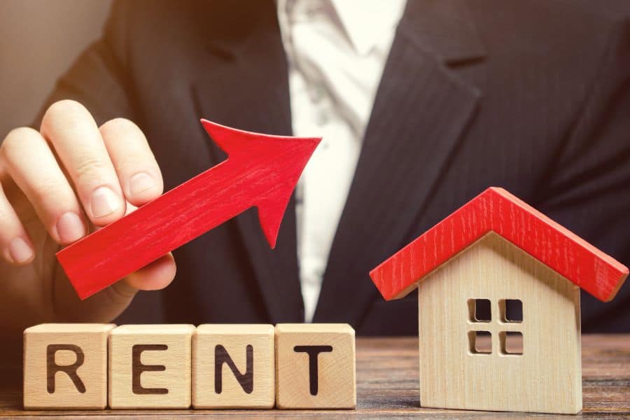 Wooden house model and rising arrow symbolising rent increase and housing payment changes.