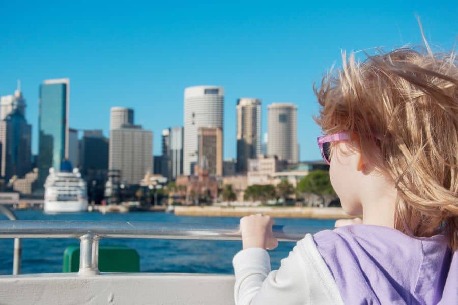 Child enjoying a ferry ride with a clear view of the Sydney CBD skyline on a sunny day.