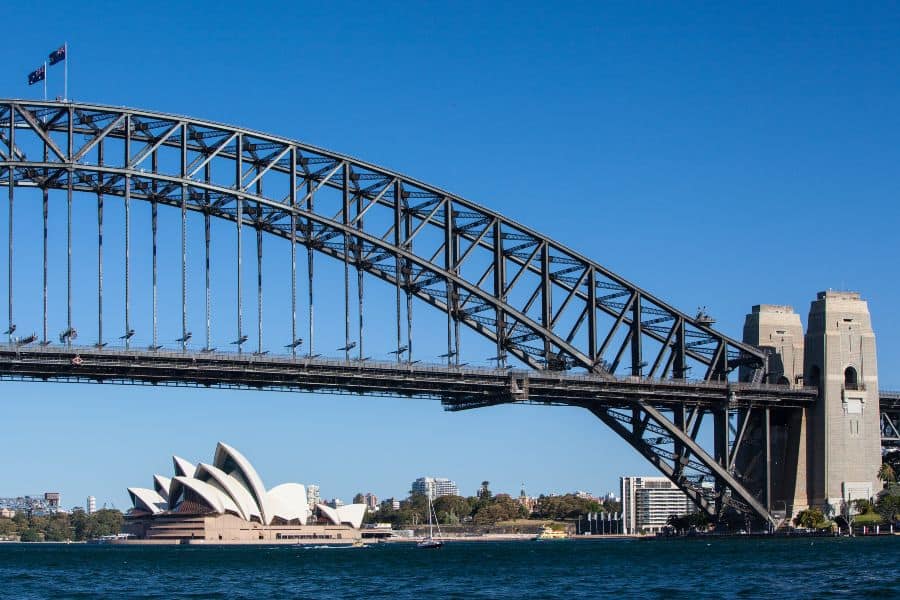 Sydney Harbour Bridge arching over the harbour with the Opera House beneath on a clear day.