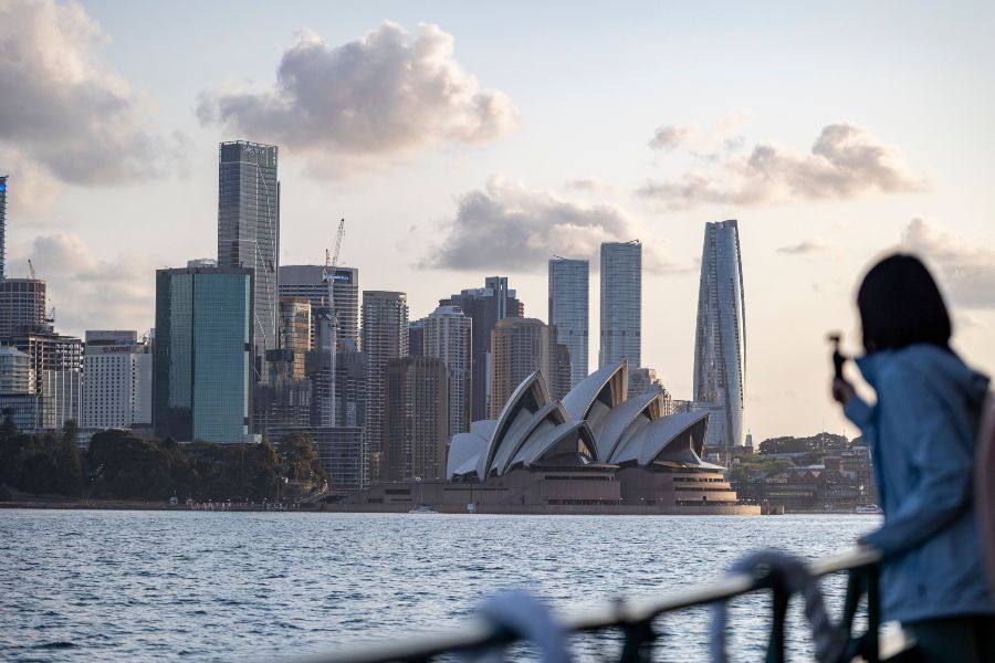 Ferry view of Sydney Opera House and CBD skyline at sunset with a person taking a photo.