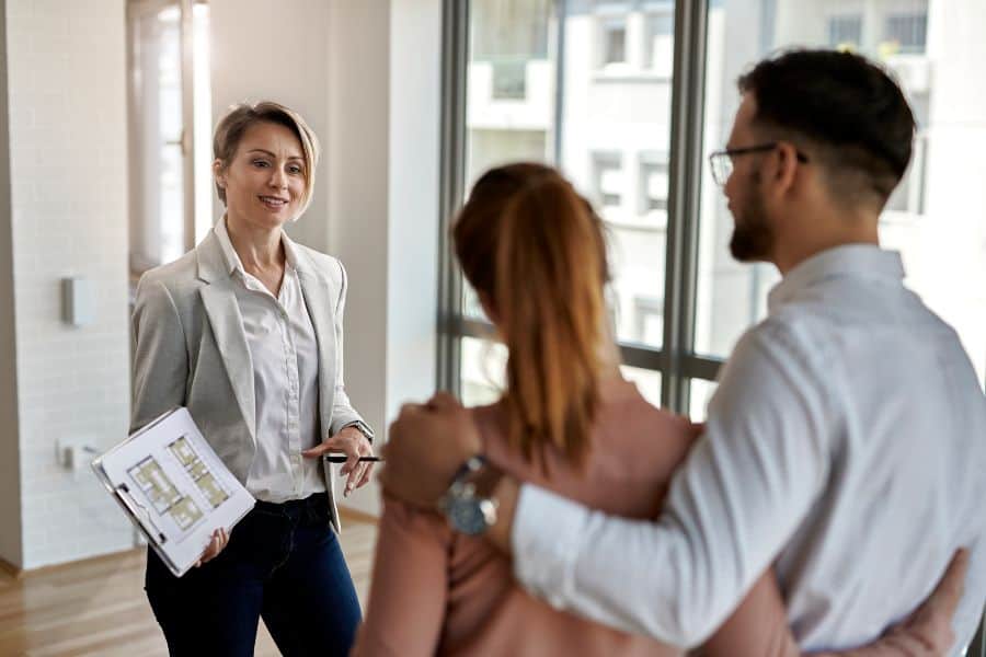 Real estate agent shows floor plans to couple in bright modern apartment.