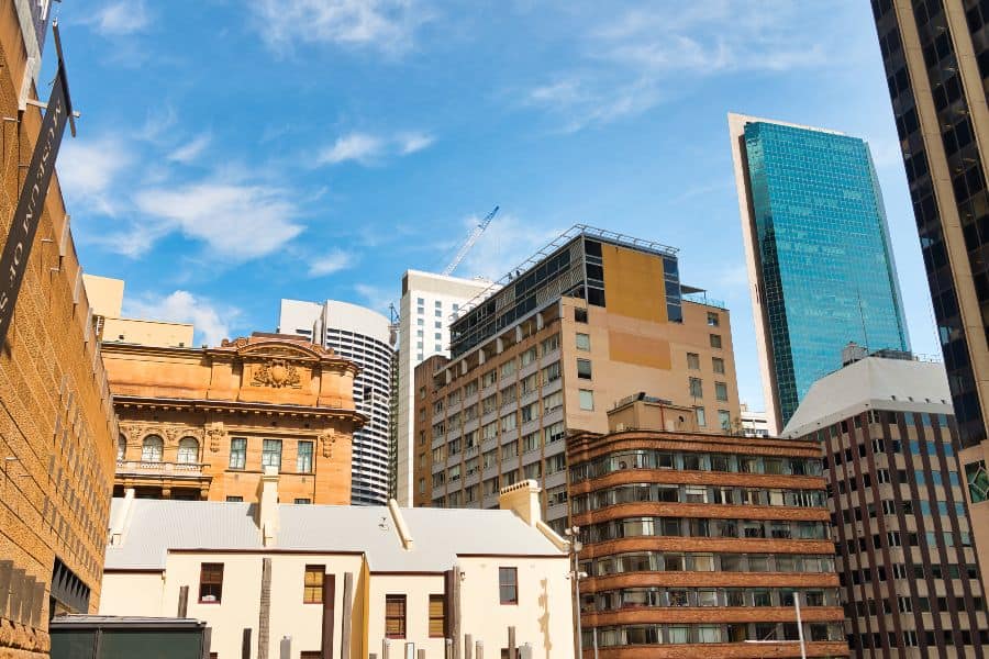 Sydney skyline with historic sandstone buildings and modern skyscrapers under blue sky.
