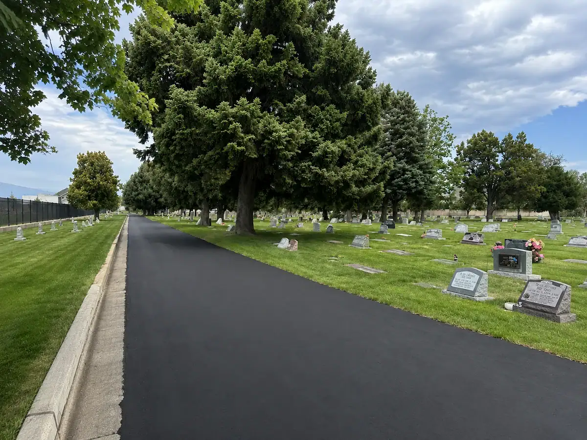 Freshly sealcoated cemetery roadway with large trees and landscaped grounds in Utah