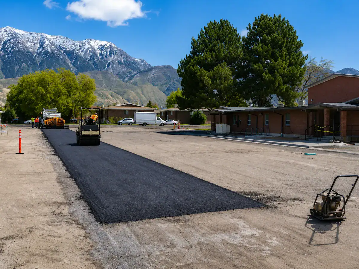 Asphalt patching and pavement repair project in a Utah parking lot with roller equipment and mountain views in the background.