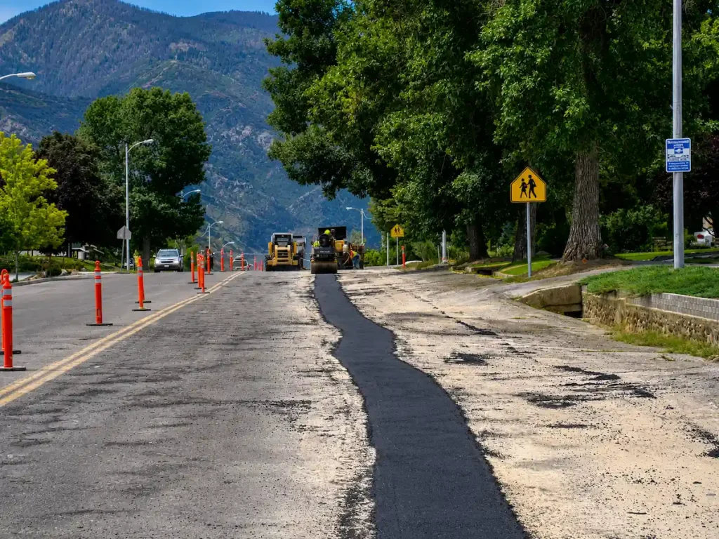 Road asphalt patching project in Utah with paving equipment and mountain backdrop