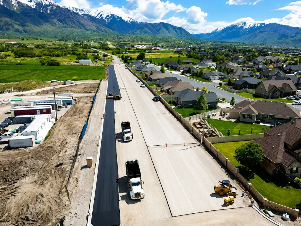 Aerial view of asphalt paving crews completing a roadway construction project in Utah with mountain views in the background.