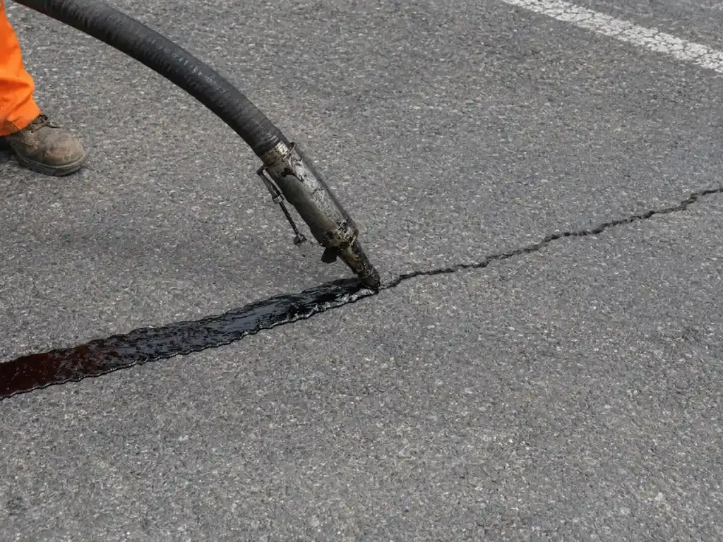 Crack sealing applicator applying fresh sealant along an asphalt crack at the EOS Fitness parking lot in Orem, Utah.