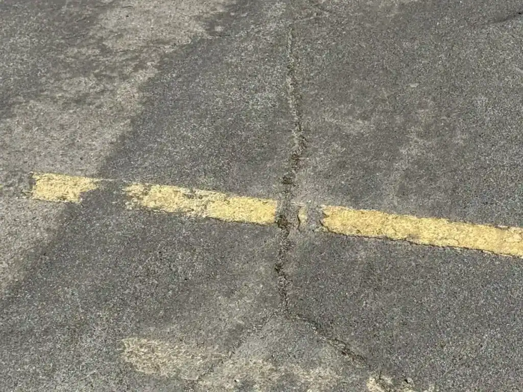 Cracked and crumbling asphalt with faded yellow markings before parking lot maintenance at Utah Valley University in Orem, Utah.
