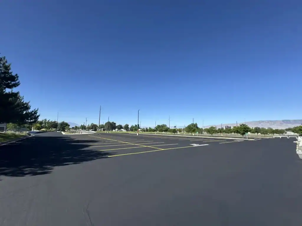 Freshly sealcoated and striped parking lot at Utah Valley University in Orem, Utah, with campus buildings and mountains in the background.