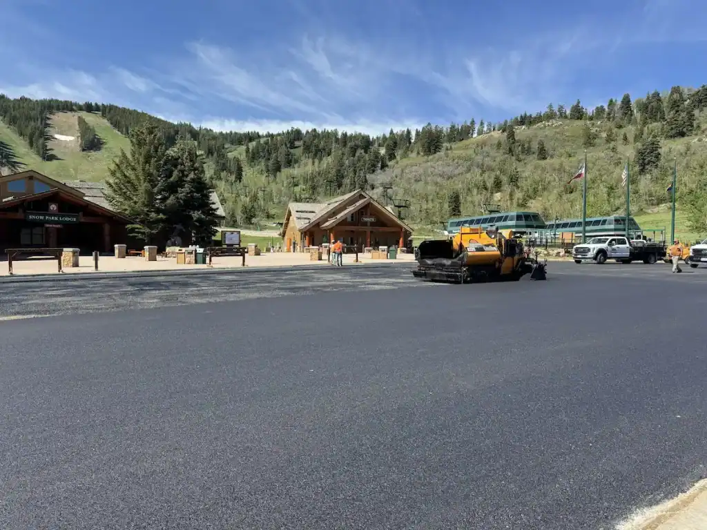 Fresh asphalt paving at Deer Valley Resort in Park City, Utah, with a paving machine and mountain scenery.