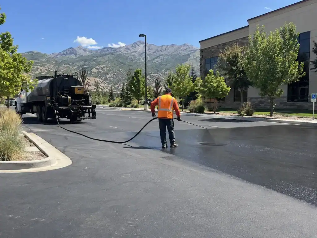 Asphalt sealcoat being applied to a commercial parking lot in Utah with mountains in the background.