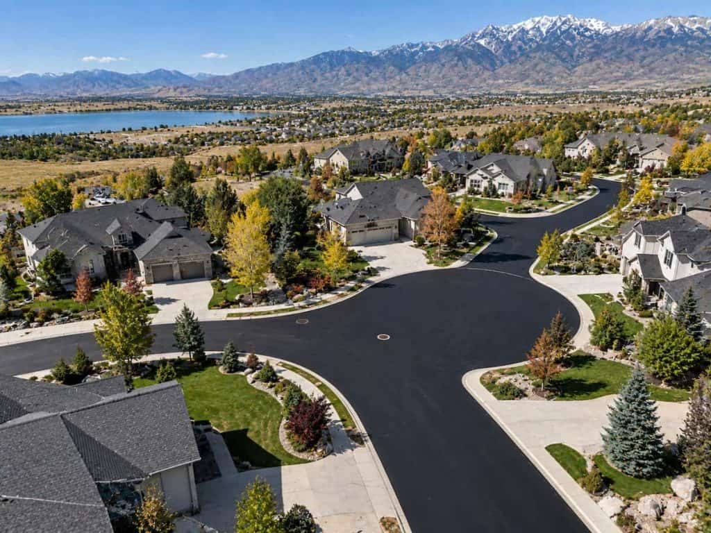 Aerial view of a Utah HOA neighborhood with freshly paved black asphalt roads and mountains in the background.