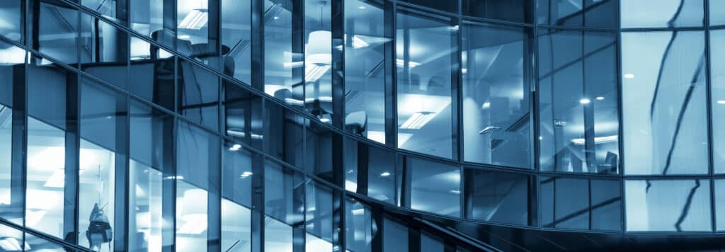 Modern glass office building with reflective windows and interior lighting.