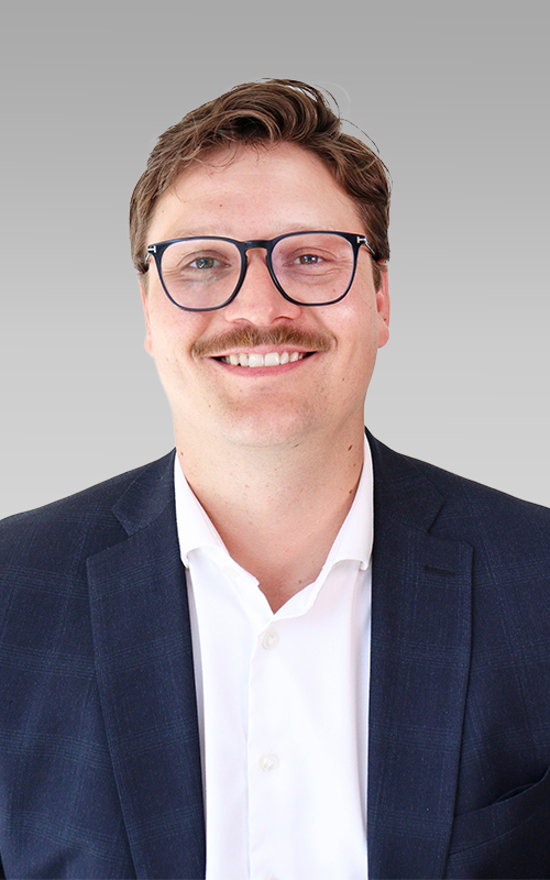 Headshot of Curtis Wispinski wearing glasses and a suit, smiling against a neutral background.