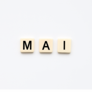 Mot « MAI » formé avec des lettres de type Scrabble beiges sur fond blanc minimaliste, représentant le mois de mai pour un article voyage « Où aller en Europe en mai ».