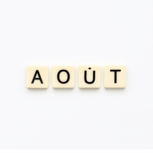 Mot « aout » formé avec des lettres de type Scrabble beiges sur fond blanc minimaliste, représentant le mois de mai pour un article voyage « Où aller en Europe en aout ».