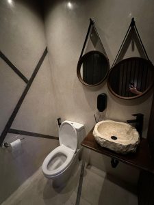 Kamar mandi minimalis dengan wastafel batu alam dan cermin bulat di restoran di Canggu.