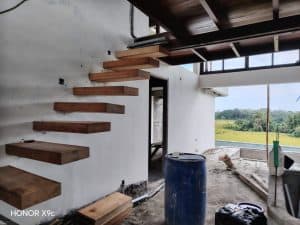 Tangga kayu di interior villa dengan pemandangan sawah dan laut di dekat Pantai Kelecung.