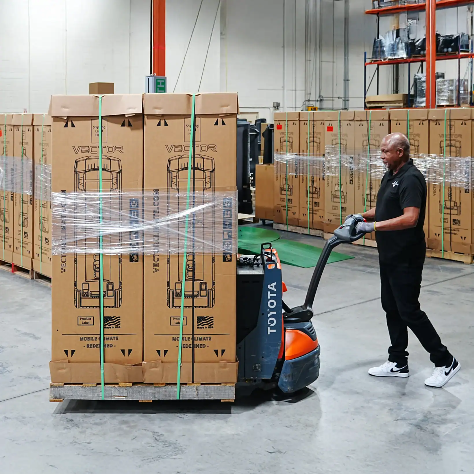 Worker moving a pallet of boxed Vector evaporative coolers in a warehouse, preparing units for shipment.