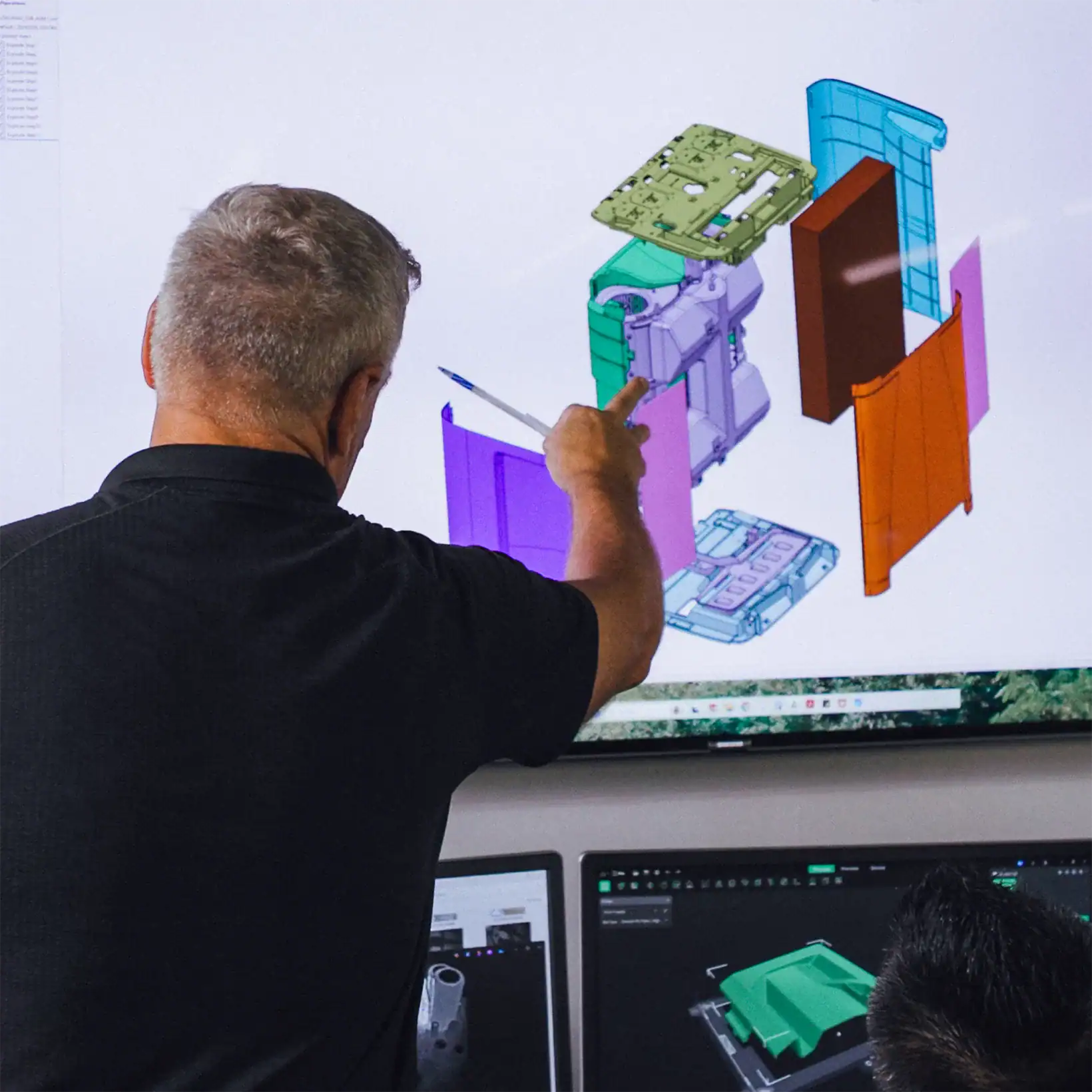 Vector team member ponting at a 3D computer model on a screen, highlighting different colored components.