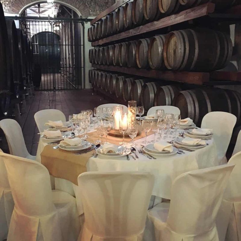 Exposição de prova de vinhos em adega histórica com barris de madeira em ambiente de estilo sofisticado e acolhedor.