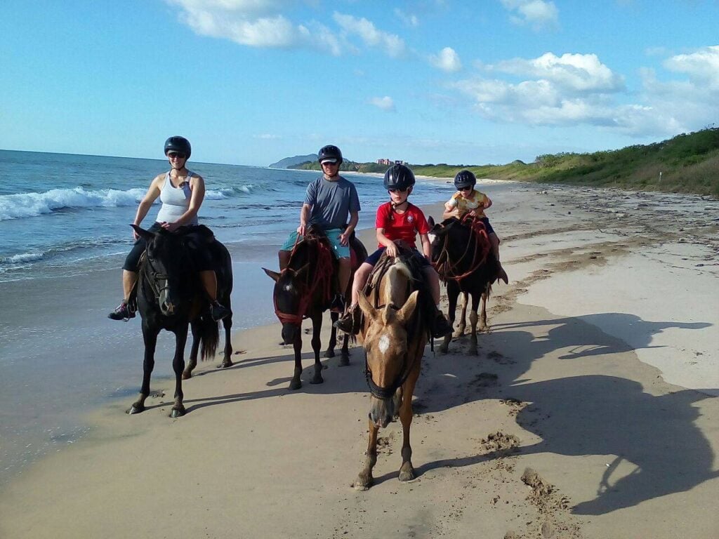 Horseback riding on the beach with a group of people enjoying a sunny day.