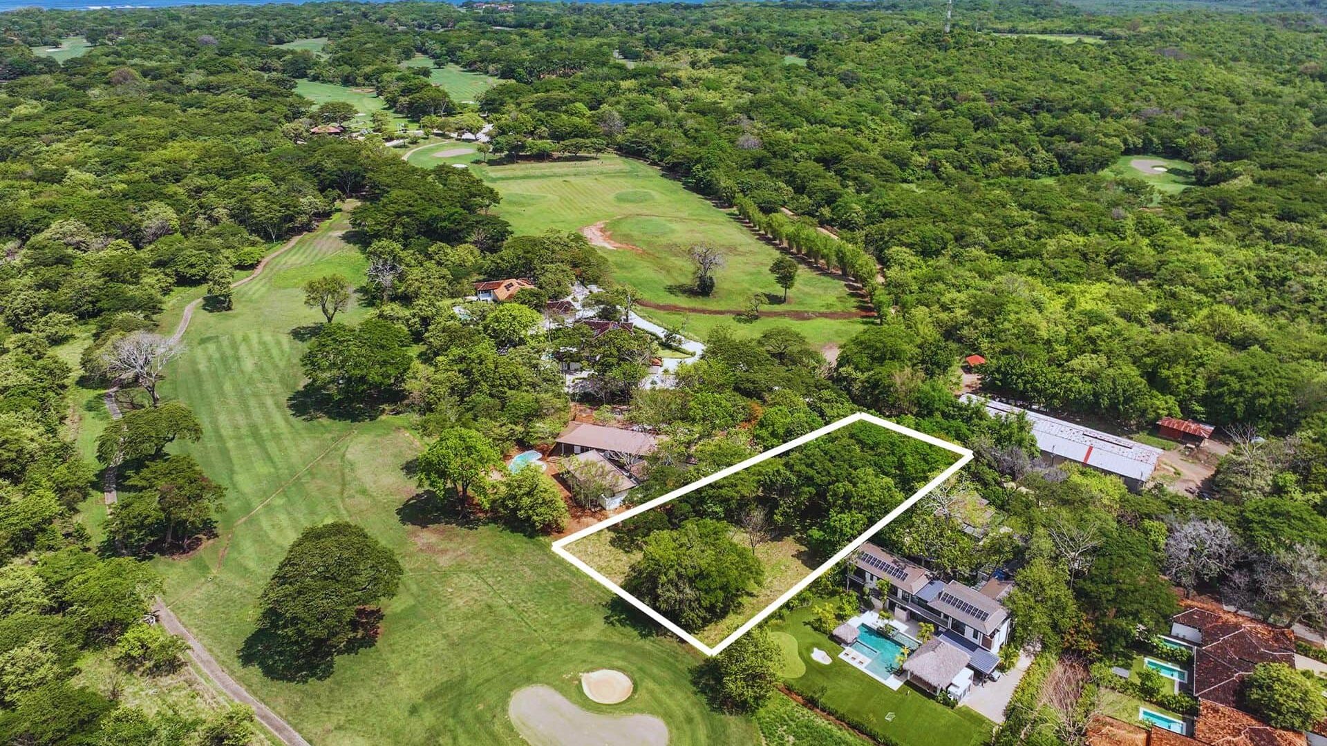 Lush green property surrounded by trees with golf course and ocean in the background.