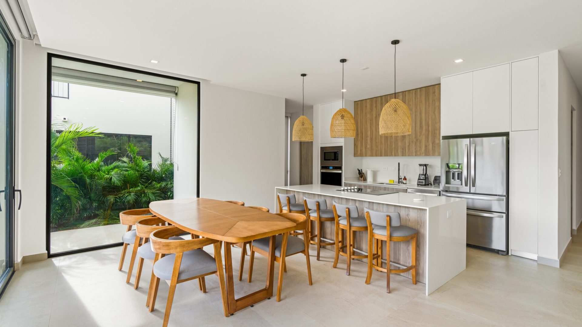 Modern kitchen and dining area with wooden accents and lush outdoor greenery.