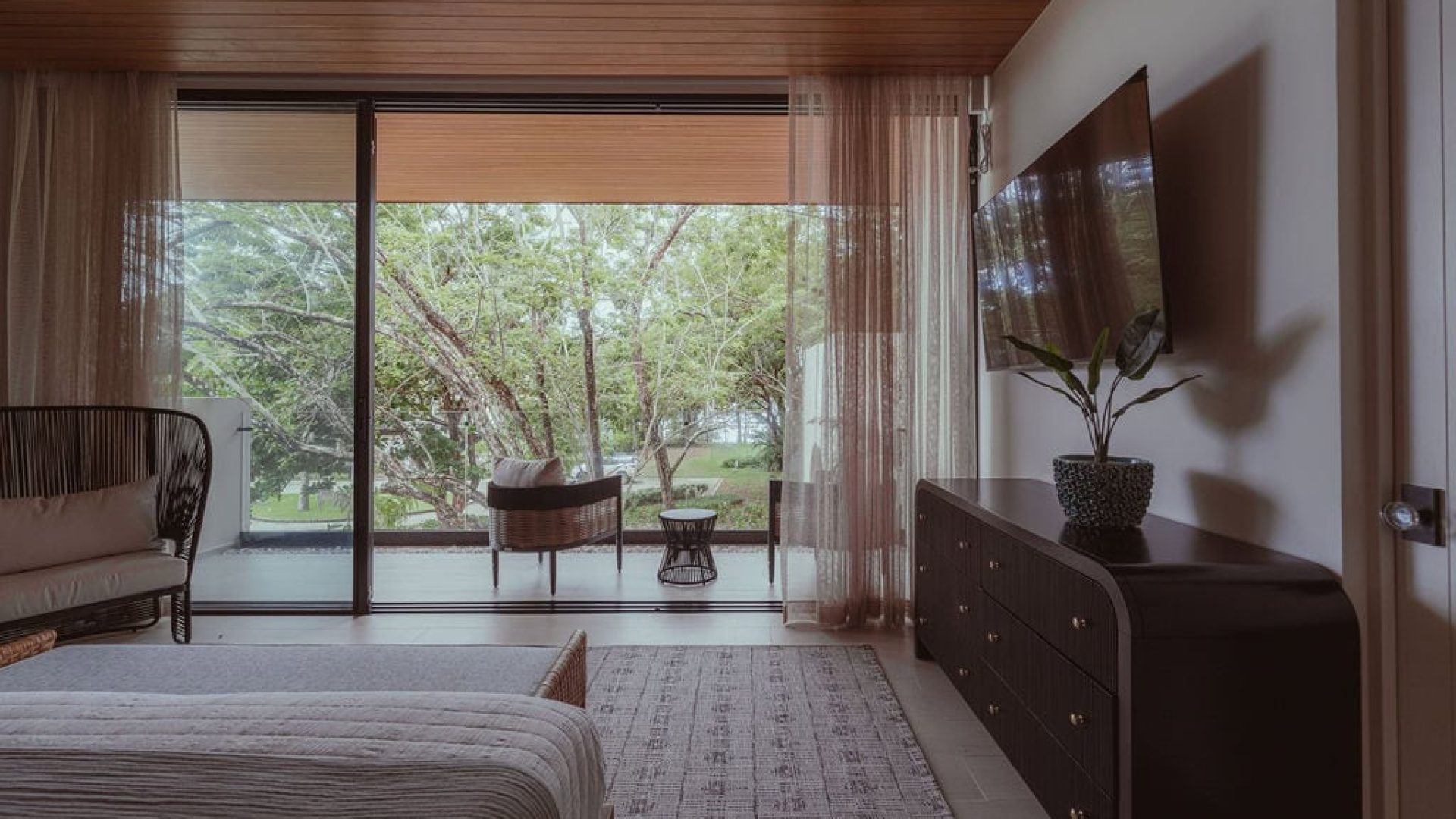 Bright modern living room with large glass sliding doors overlooking lush greenery and outdoor seating area.